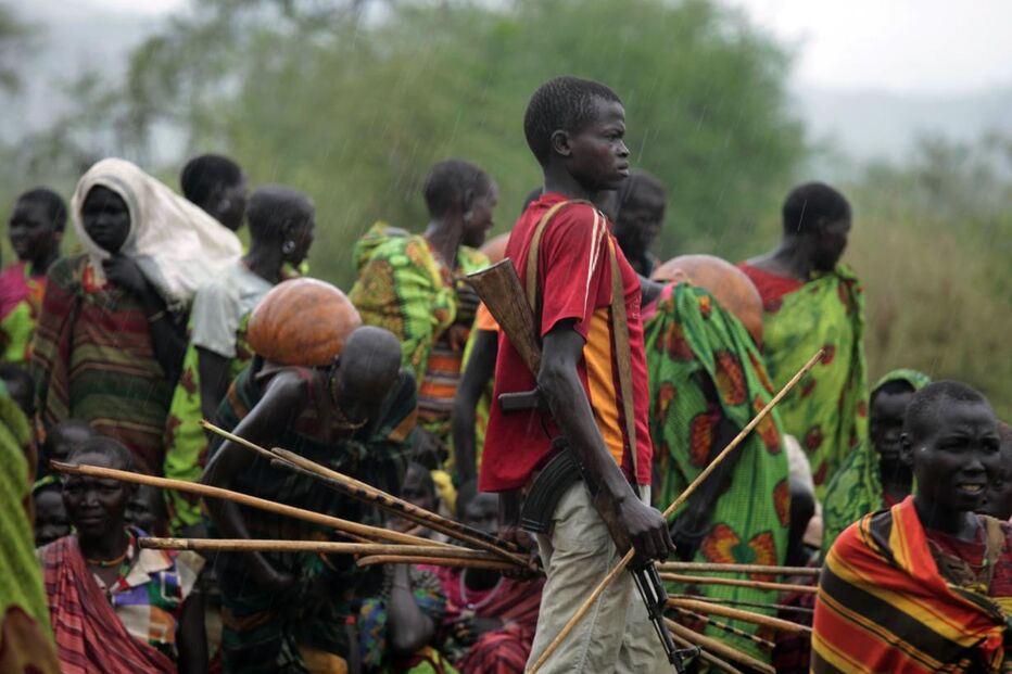 Um homem armado anda frente dos membros da tribo Dadinga enquanto aguardam pelos alimentos distribuídos pelas equipas de ajuda humanitária na aldeia de Lauro, sul do Sudão. (goran Tomasevic, Reuters)