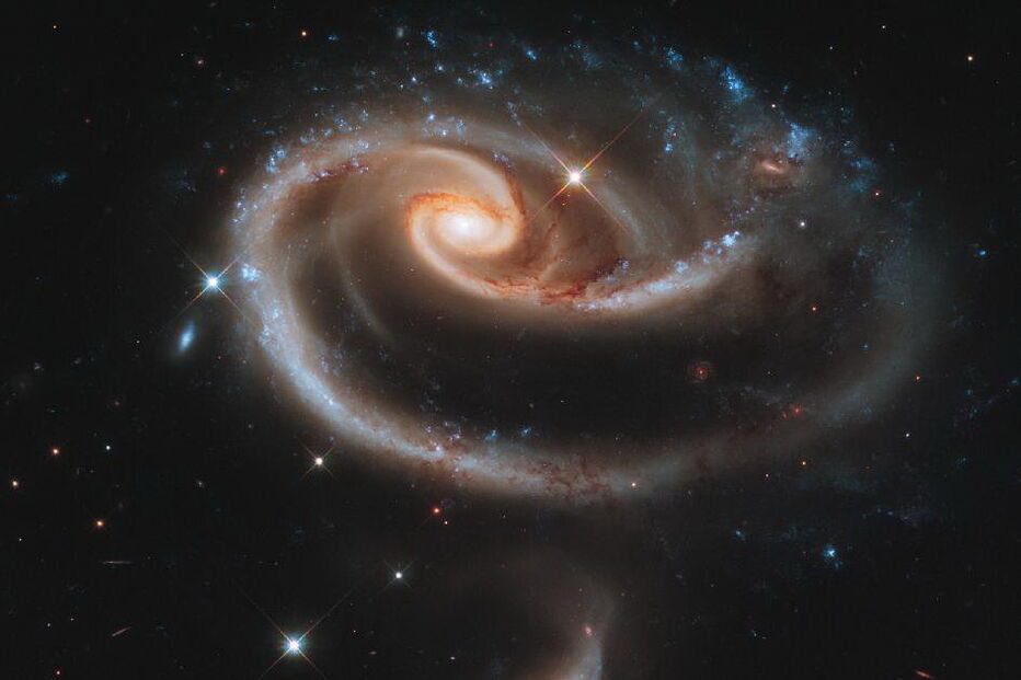 Para celebrar o 21.º aniversário do lançamento do telescópio espacial ‘Hubble’, os astrónomos do Space Telescope Science Institute direccionaram o ‘Hubble’ para fotografar o conjunto de galáxias designadas por Arp 273. Este conjunto é constituído por uma grande galáxia espiral, chamada UGC 1810, com um disco que está distorcido, ganhando o formato de uma rosa. A distorção resulta da atracção gravitacional de maré da galáxia, conhecida como UGC 1813. (direitos reservados)