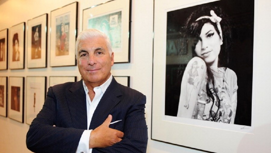 Mitch Winehouse posa junto a uma fotografia da falecida filha