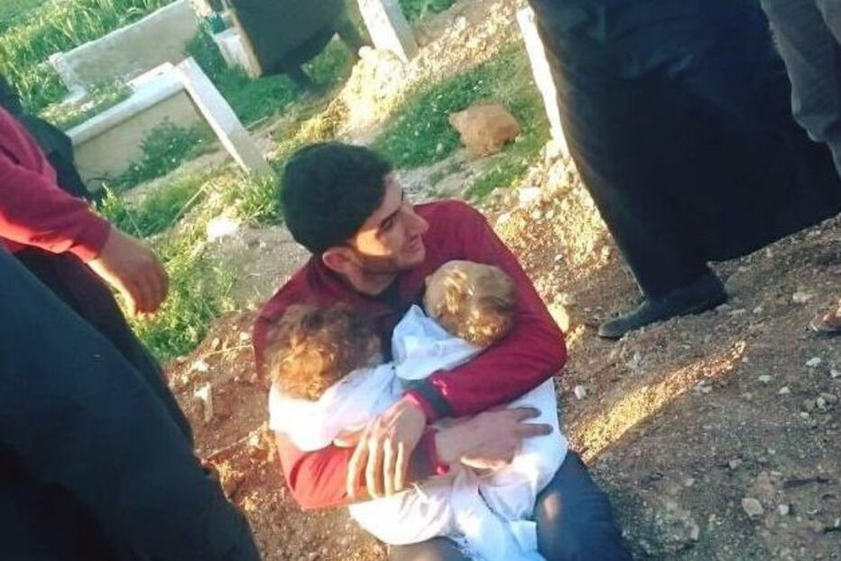 Pai segura nos braços os seus dois filhos mortos