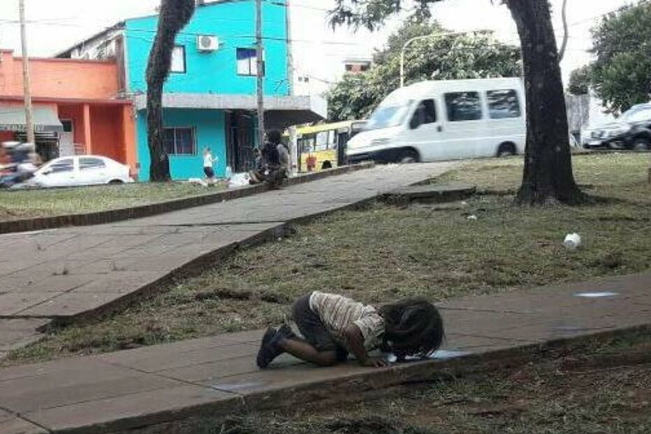 Menina bebe água de um charco na rua