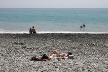 Adeptos aproveitam o calor para estar na praia em frente ao estádio Fisht, em Sochi.