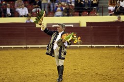 O toureiro/cavaleiro tauromáquico com flores nas mãos acena e agradece ao público na arena