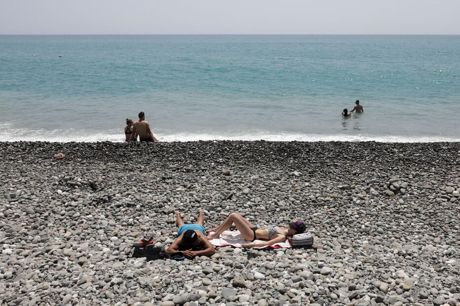 Adeptos aproveitam o calor para estar na praia em frente ao estádio Fisht, em Sochi.
