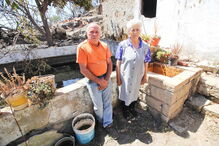 José Eduardo, 60 anos, com a mãe, Maria Margarida, de 83, junto à casa e ao tanque de onde o morador retirou água com baldes para salvar a habitação e animais