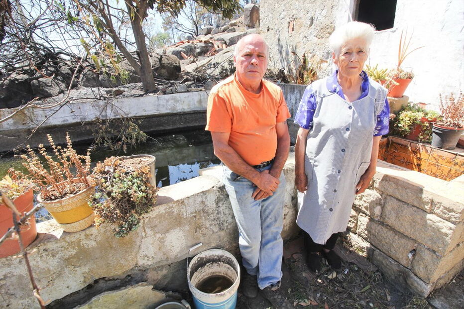 José Eduardo, 60 anos, com a mãe, Maria Margarida, de 83, junto à casa e ao tanque de onde o morador retirou água com baldes para salvar a habitação e animais