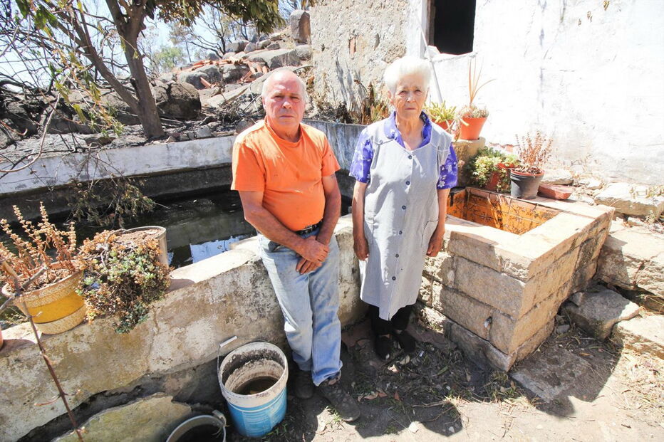 José Eduardo, 60 anos, com a mãe, Maria Margarida, de 83, junto à casa e ao tanque de onde o morador retirou água com baldes para salvar a habitação e animais