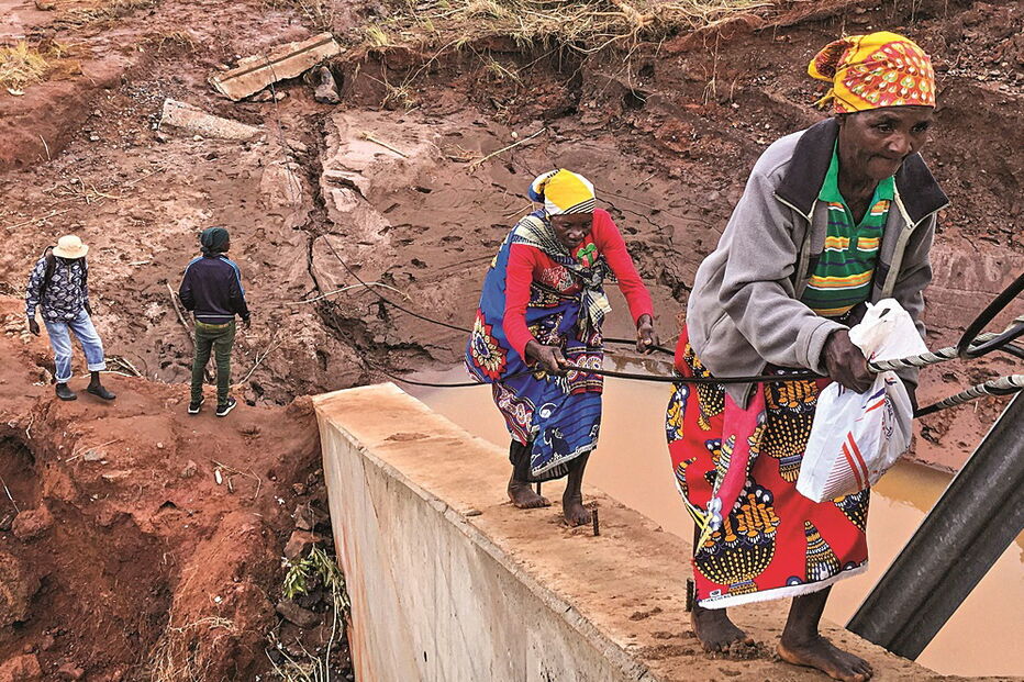 Pessoas atravessam o rio Muhinga usando uma ponte danificada