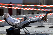 Homem protegido com máscara e óculos apanha apanha sol enquanto lê um livro durante pandemia em Dresden, na Alemanha