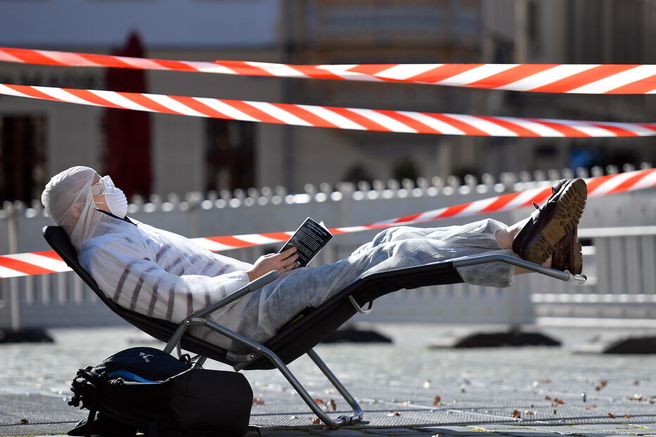 Homem protegido com máscara e óculos apanha apanha sol enquanto lê um livro durante pandemia em Dresden, na Alemanha