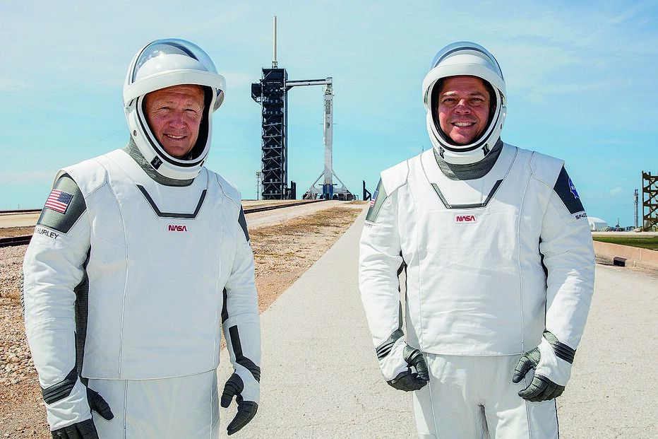 Os astronautas da NASA Doug Hurley (esquerda) e Bob Behkem com o foguetão Falcon 9, da empresa privada SpaceX, ao fundo 