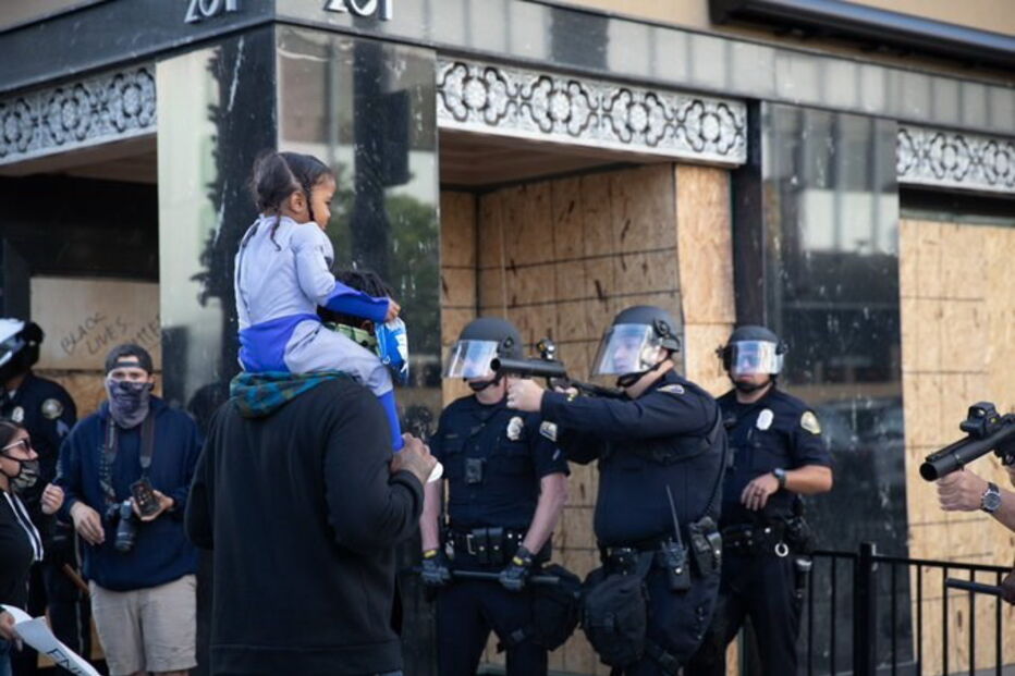 Foto mostra polícia de arma apontada a criança às cavalitas do pai