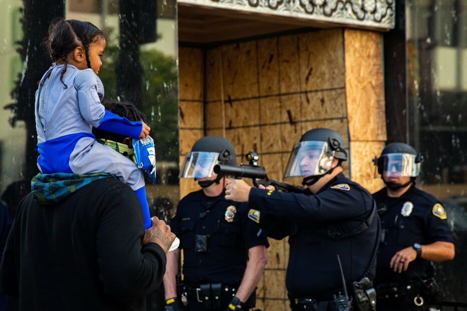 Foto mostra polícia de arma apontada a criança às cavalitas do pai