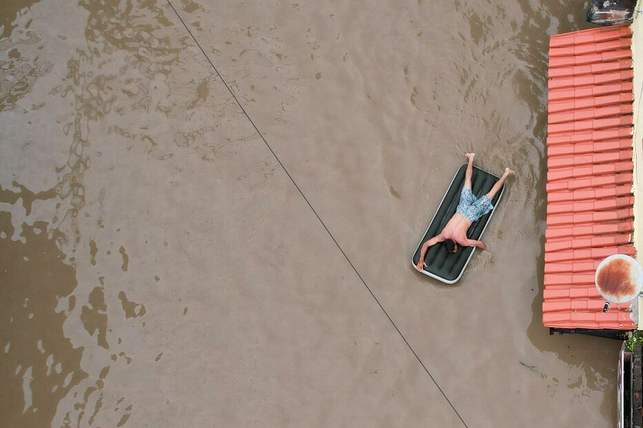 Homem rema num colchão insuflável para tentar chegar a uma casa.