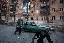 Um homem caminha ao lado de um carro danificado durante um ataque militar em Kiev