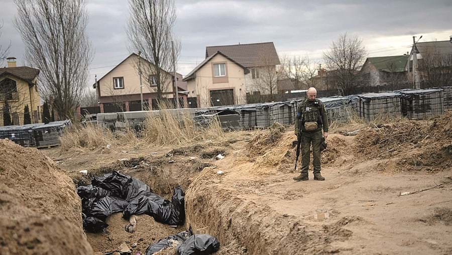 Soldado ucraniano presta homenagem às vítimas civis que jazem numa vala comum em Bucha