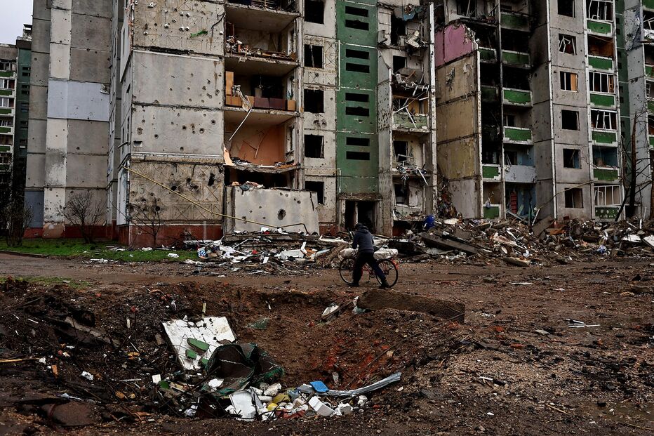 Homem passa de bicicleta por uma cratera e um prédio destruído por bombardeamentos, em Chernihiv