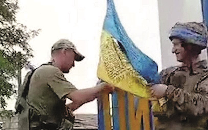 Militares ucranianos hasteiam a bandeira nacional junto à placa com o nome da cidade de Lyman, na região de Donetsk 