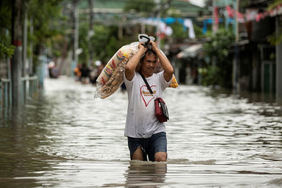 Um vendedor carrega produtos alimentares enquanto caminha por uma rua inundada após fortes chuvas trazidas pela tempestade tropical Nalgae, em Imus, província de Cavite, Filipinas