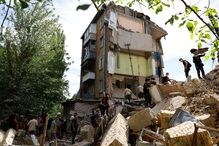 Residentes locais ajudam os socorristas a remover os destroços de um edifício de apartamentos danificado durante os ataques de mísseis russos, em Kiev