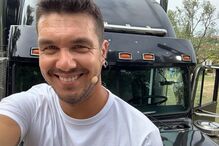 Homem sorri em frente a um camião preto com microfone