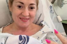 Mulher sorri numa cama de hospital e faz um sinal de paz