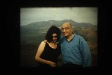 Uma mulher e um homem sorriem para a câmara com montanhas ao fundo.
