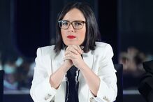 Uma mulher de óculos e blazer branco com as mãos juntas