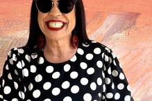 Mulher sorri com batom vermelho, óculos de sol e vestido de bolinhas