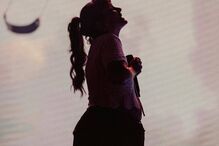 Silhueta de Lorde durante apresentação, com microfone e rabo de cavalo