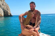 Casal relaxa num barco com água azul e montanhas ao fundo