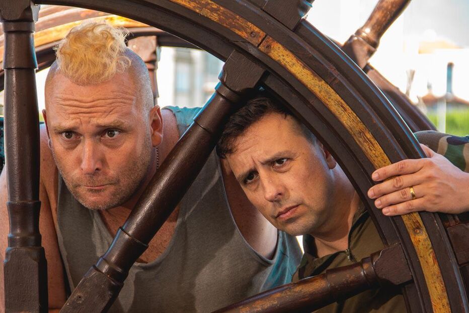 Dois homens posam atrás do leme de um barco