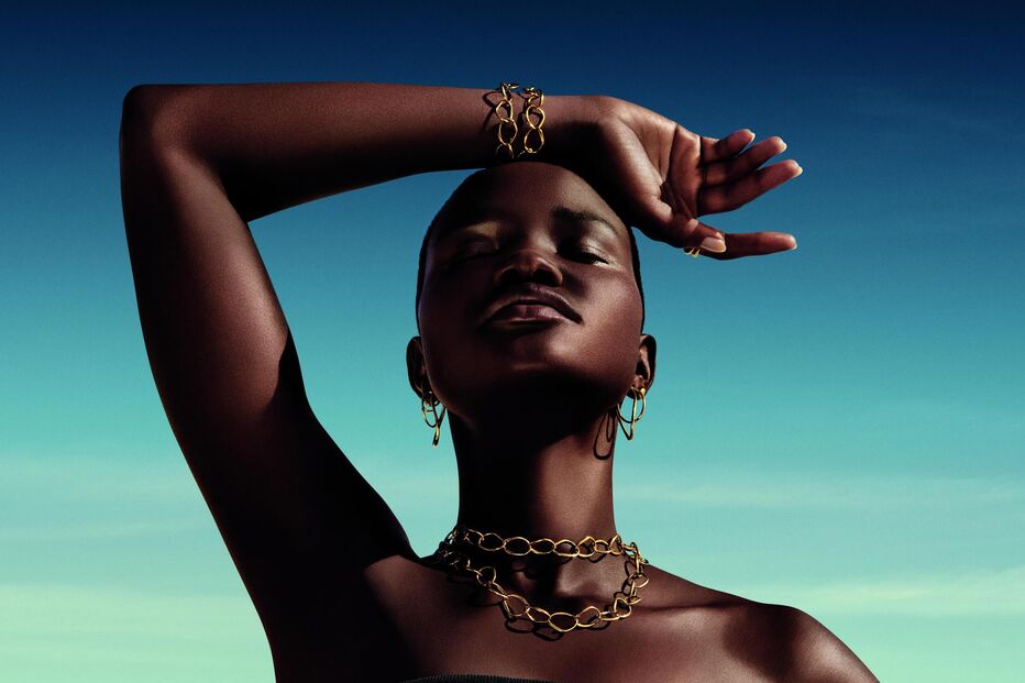 Mulher negra exibe colar, brincos e pulseira dourados sob um céu azul