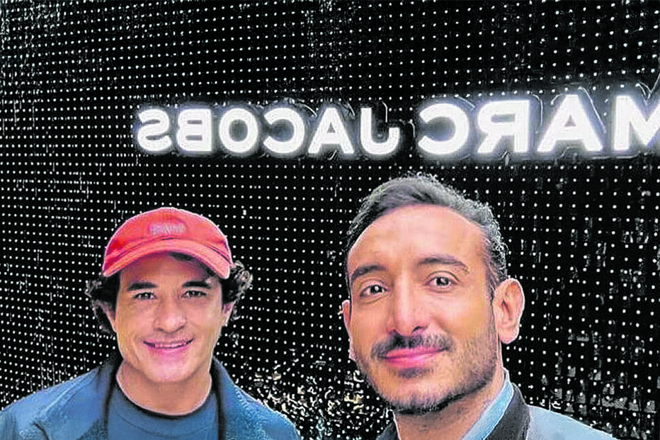 Dois homens posam para foto com o logo da marca Marc Jacobs ao fundo