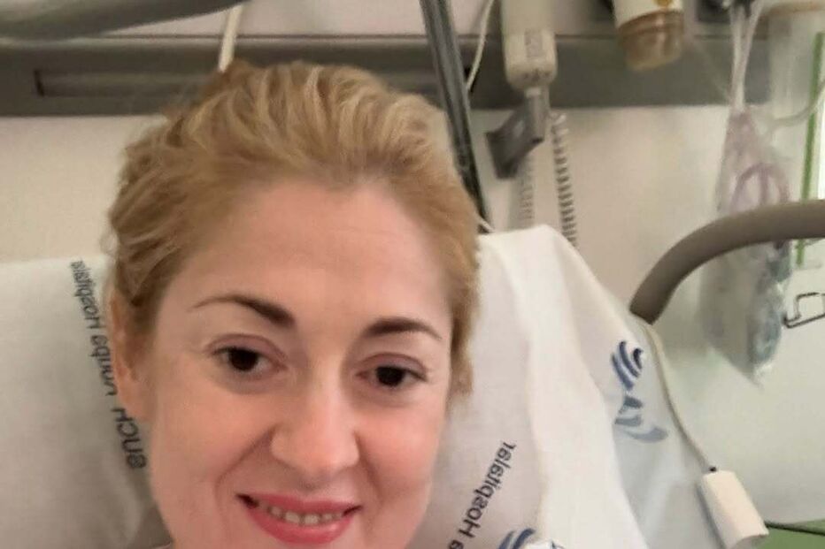 Mulher sorri na cama de hospital e faz sinal de paz com a mão