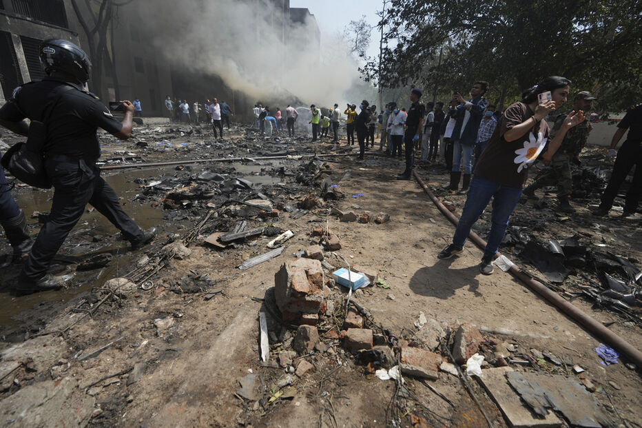 Após explosão, destroços e fumo são visíveis numa rua, enquanto pessoas observam