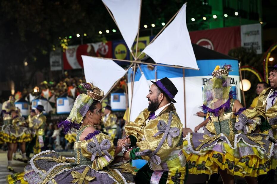 Grupo folclórico exibe trajes tradicionais com um moinho de vento ao fundo