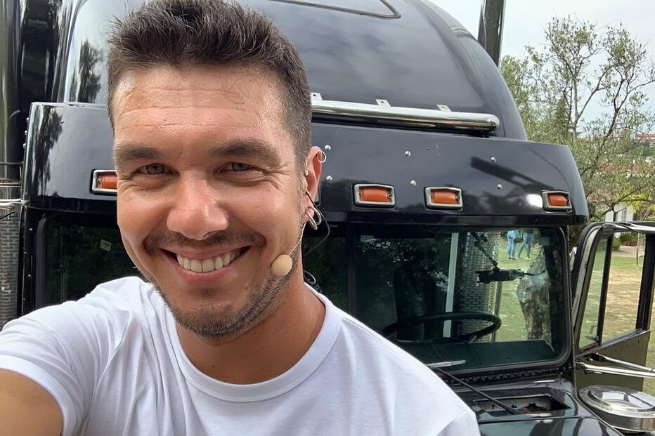 Homem sorri em frente a um camião preto com microfone