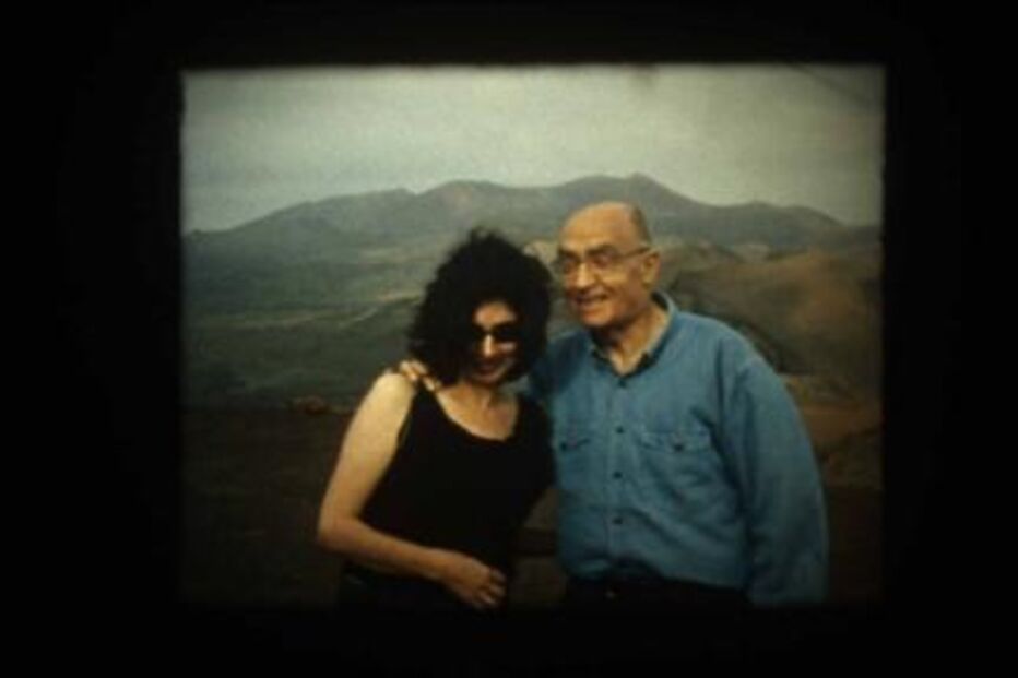 Uma mulher e um homem sorriem para a câmara com montanhas ao fundo.
