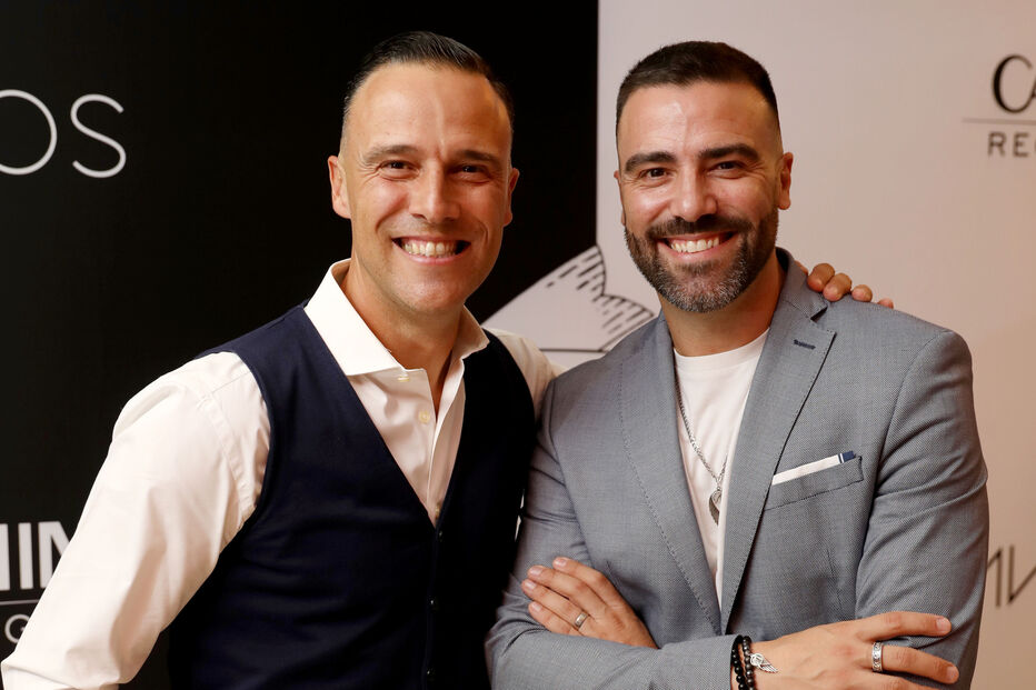 Dois homens posam juntos, sorrindo para a câmara