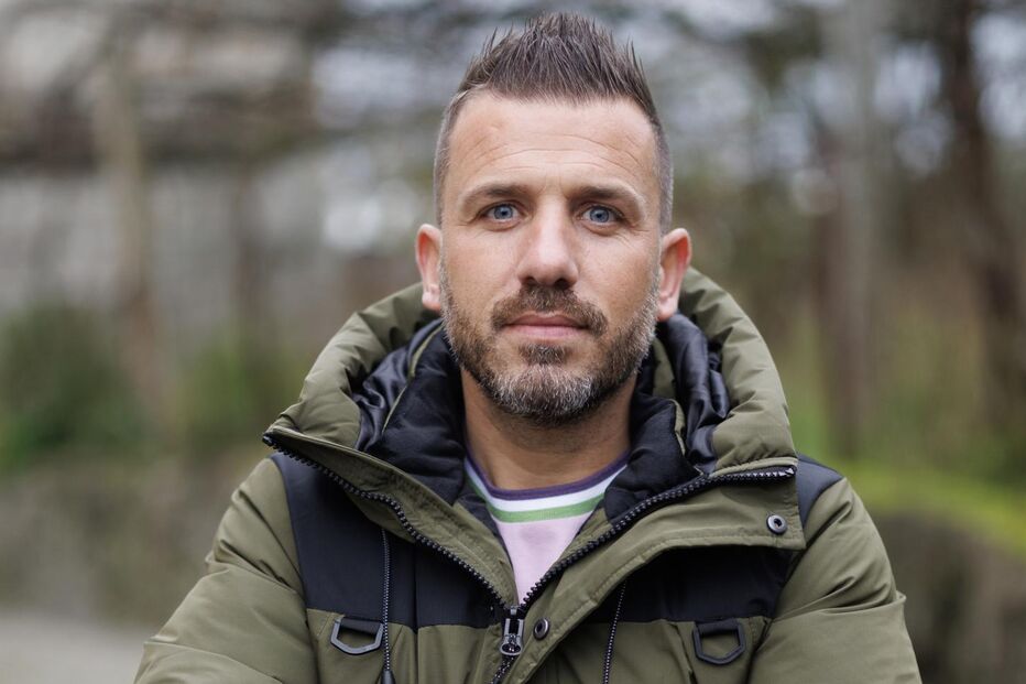 Homem de barba e casaco verde olha para a câmara