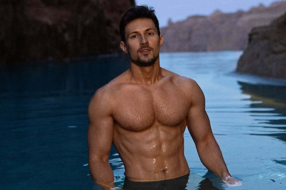 Homem emerge da água calma num cenário montanhoso, exibindo físico definido