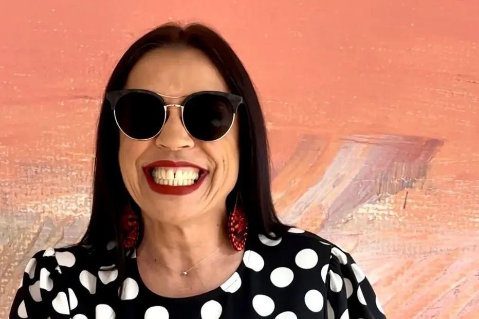 Mulher sorri com batom vermelho, óculos de sol e vestido de bolinhas