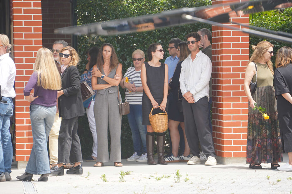 Pessoas reunidas ao ar livre, algumas com óculos de sol e outras a segurar flores