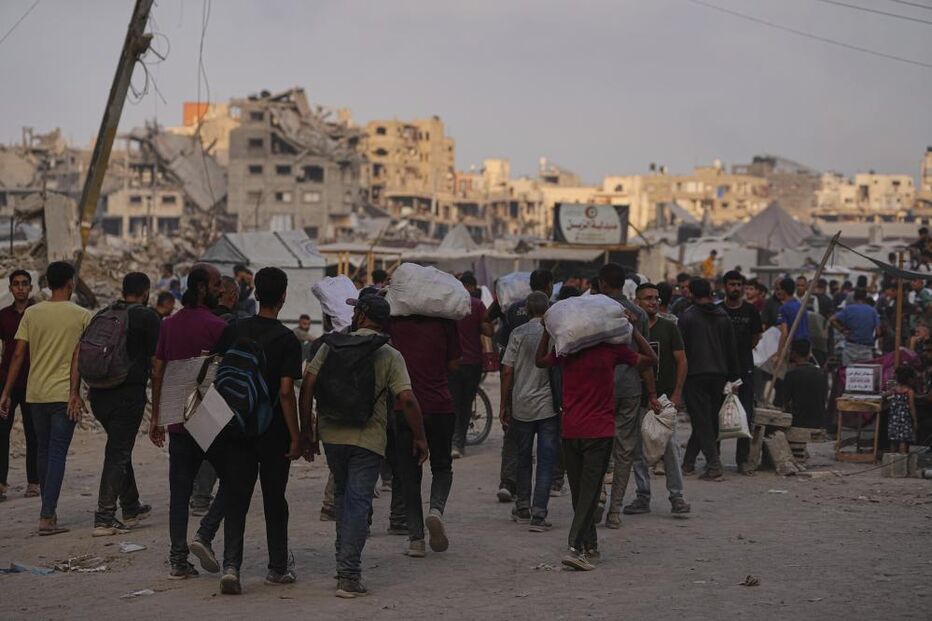 Pessoas carregam sacos numa rua com edifícios destruídos em Gaza