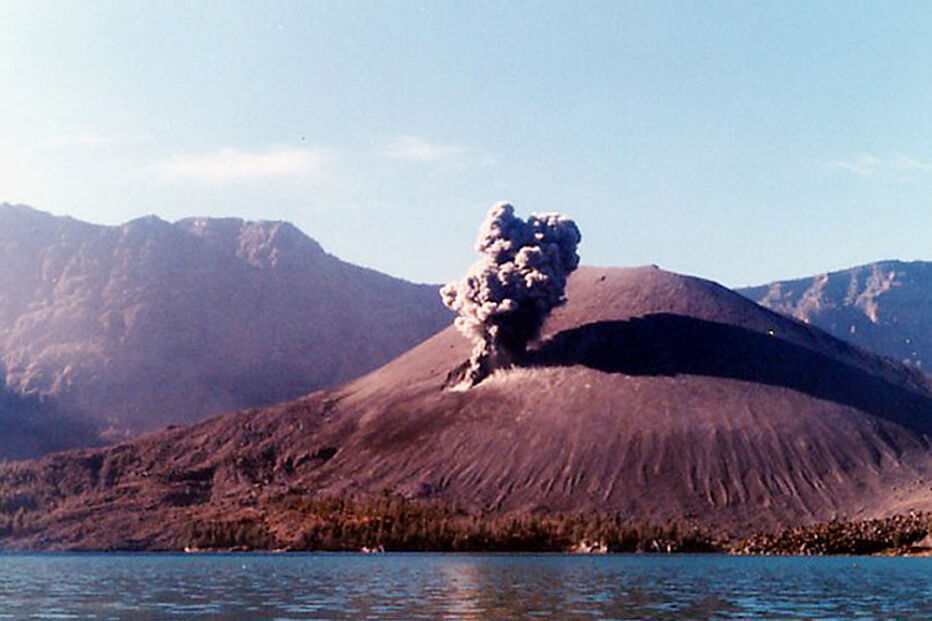 Erupção vulcânica junto a um lago e montanhas