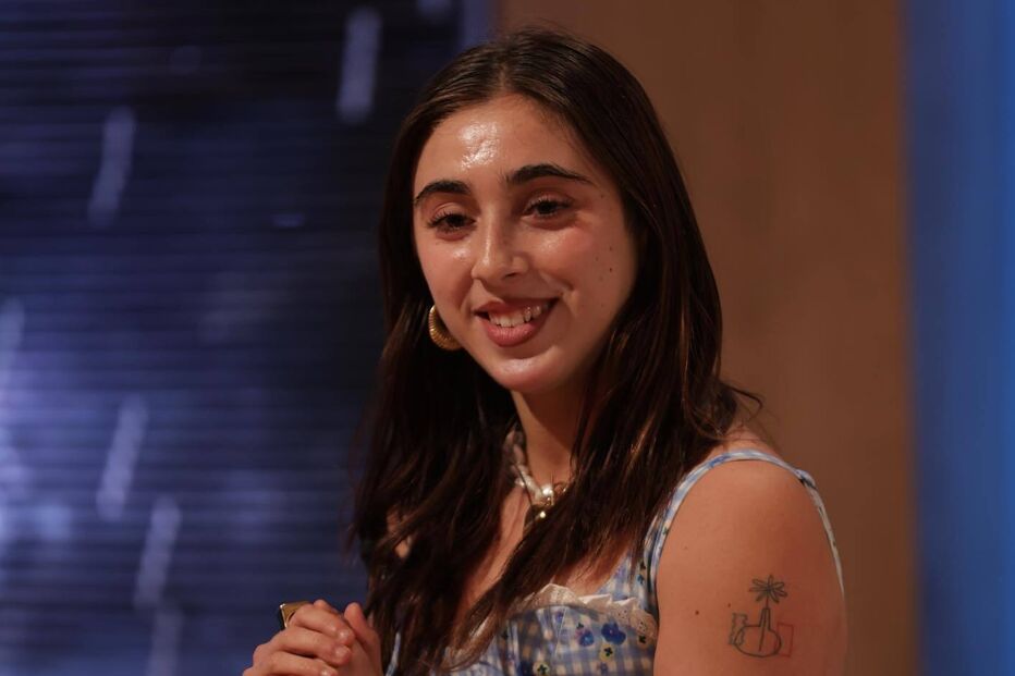 Mulher sorri com vestido de quadrados azuis e tatuagens no braço