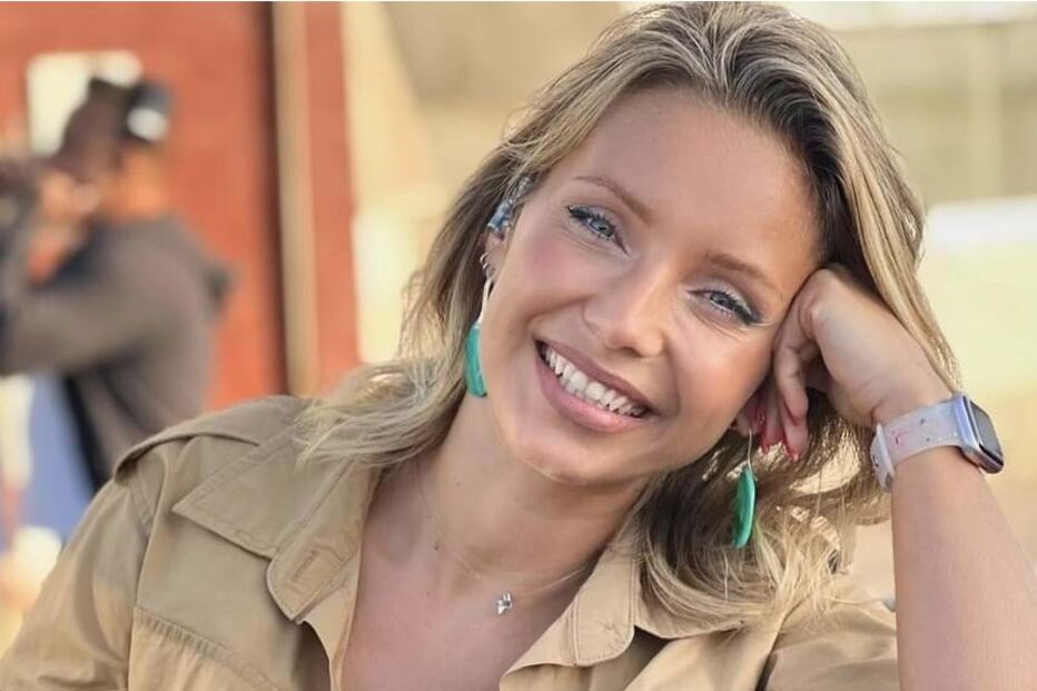 Mulher sorri para a câmara com blusa azul e casaco bege