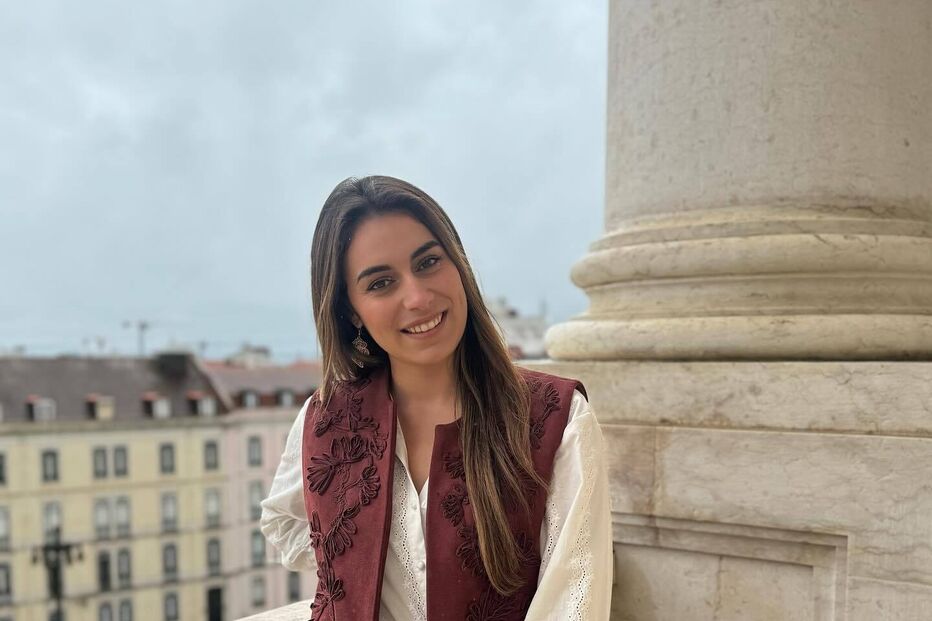 Mulher sorri com colete bordado, camisa branca e calças de ganga em Lisboa