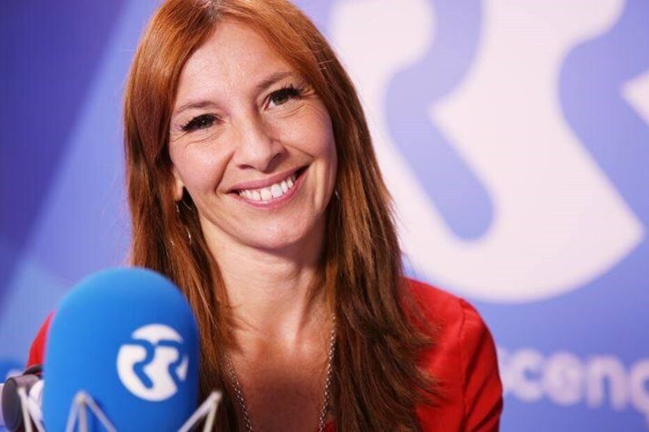 Mulher sorri para a câmara num estúdio de rádio.
